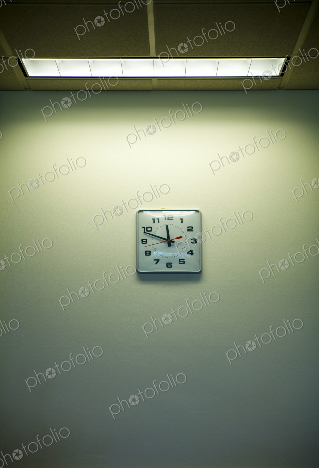 Clock on an office wall under a strip light, time nearly 11.50. Clockwatching.