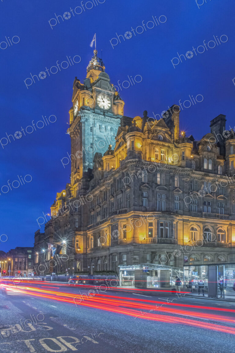 Clock tower of Balmoral Hotel lit up at night with traffic light blur below.