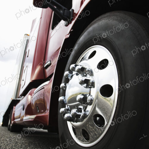 Close up 3/4 angle view of the cab and front tire on a commercial truck on the road at… Close up 3/4 angle view of the cab and front tire on a commercial truck on the road at…
