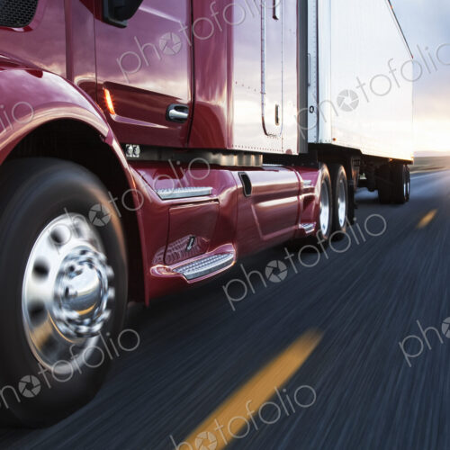 Close up 3/4 angle view of the cab and front tire on a commercial truck on the road at…