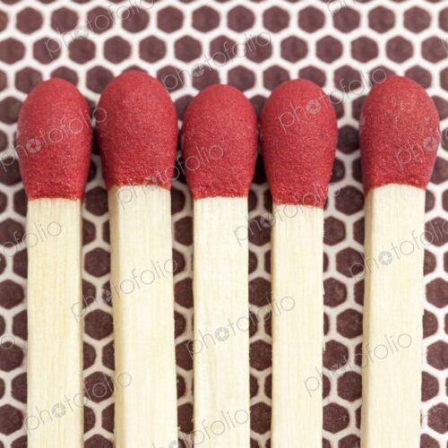 Close-up macro image of five unlit wooden matchsticks with red heads arranged side by…