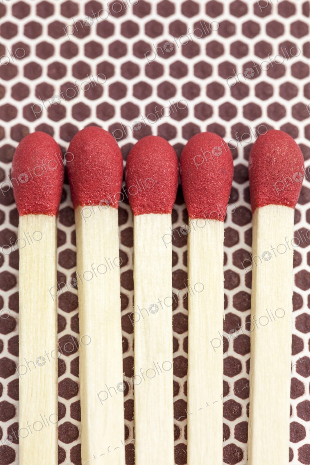 Close-up macro image of five unlit wooden matchsticks with red heads arranged side by…