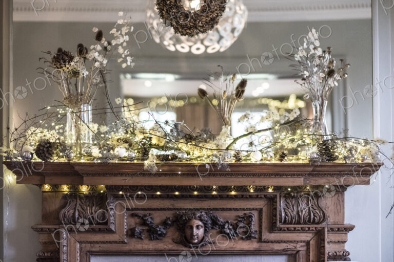 Close up of Christmas decorations on beautifully carved wooden mantelpiece, mirror above.