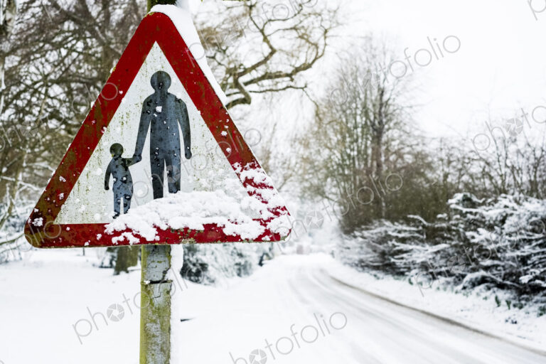 Close up of a 'Pedestrians in road' sign on side of snow-covered rural road.
