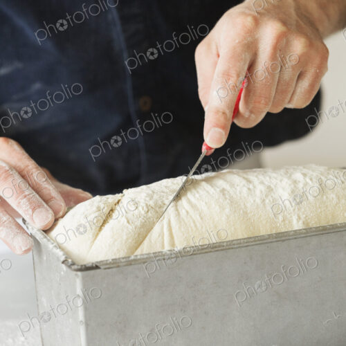 Close up of a baker cutting bread dough in a baking tin.