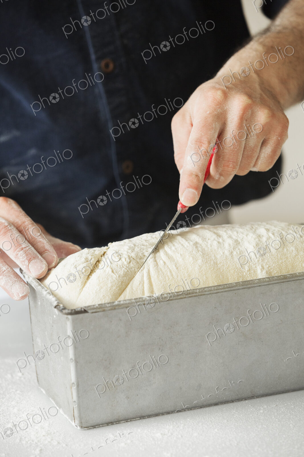 Close up of a baker cutting bread dough in a baking tin.