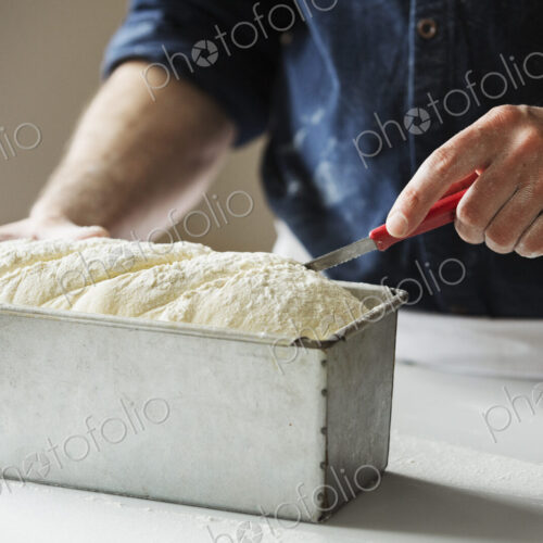Close up of a baker cutting bread dough in a baking tin.