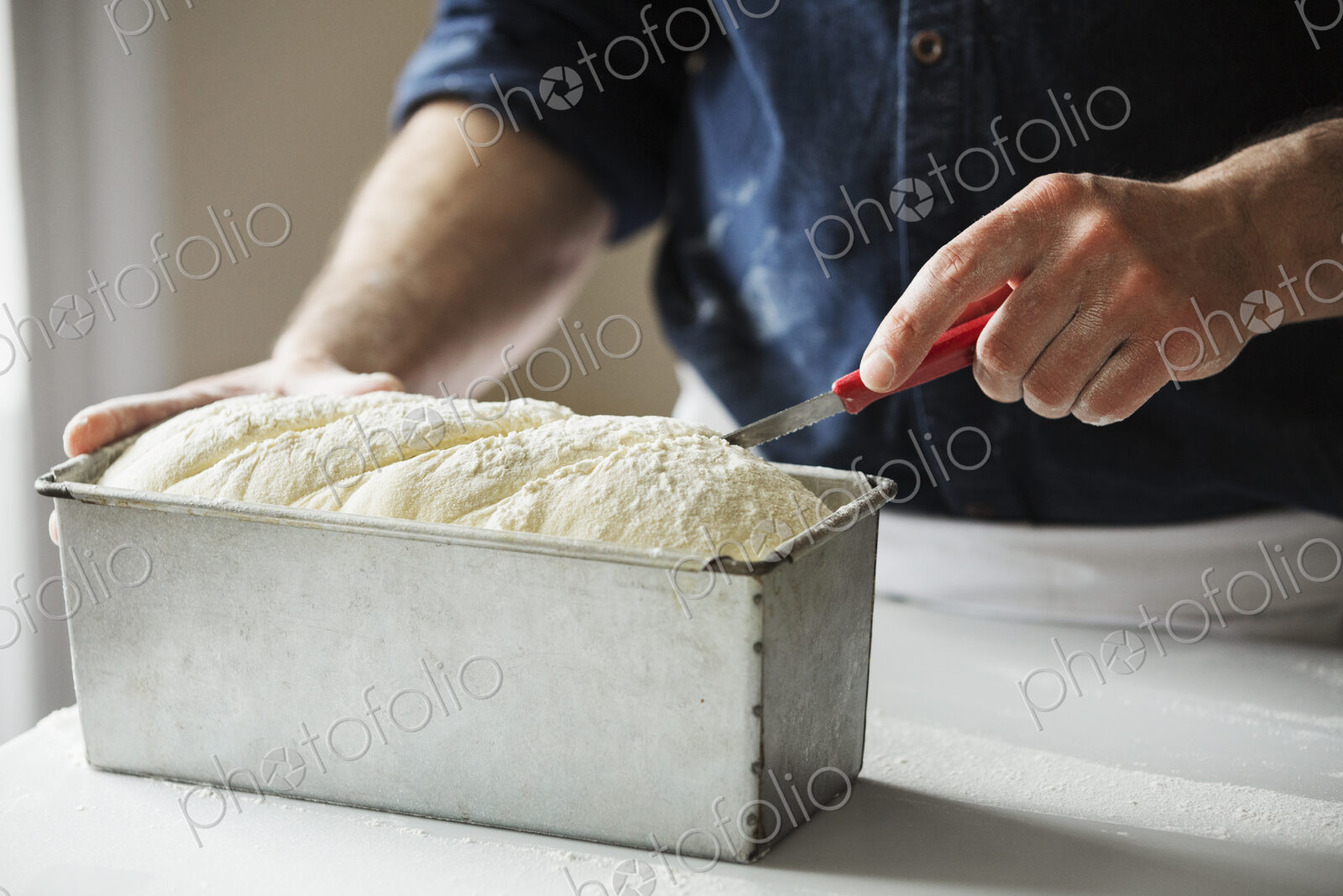 Close up of a baker cutting bread dough in a baking tin.