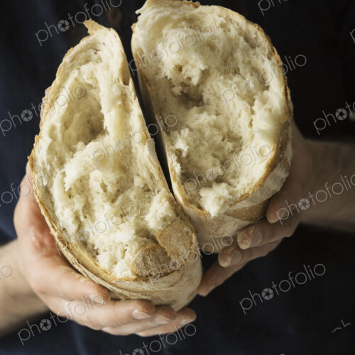 Close up of a baker holding a fresh baked white bread loaf torn in half.