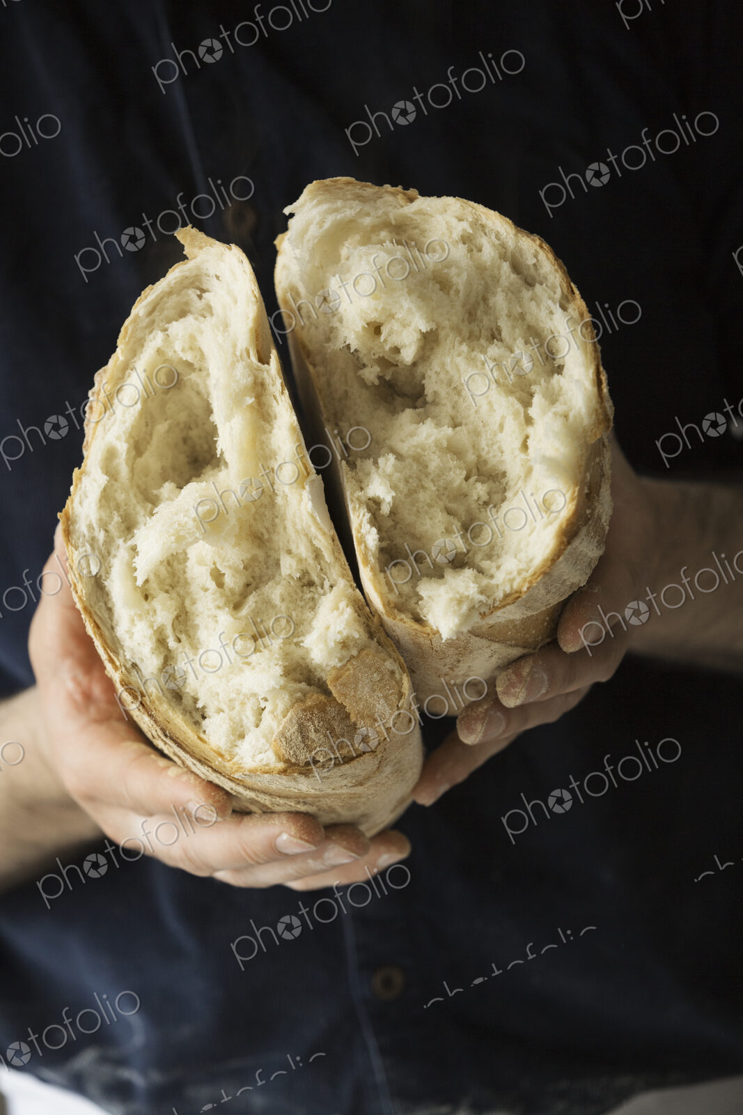 Close up of a baker holding a fresh baked white bread loaf torn in half.