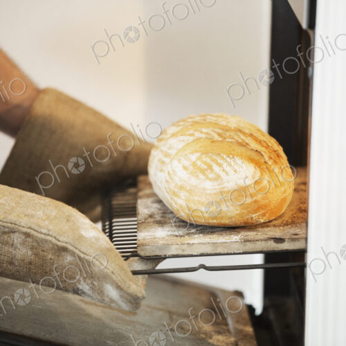 Close up of a baker taking a freshly baked loaf bread out of an oven.