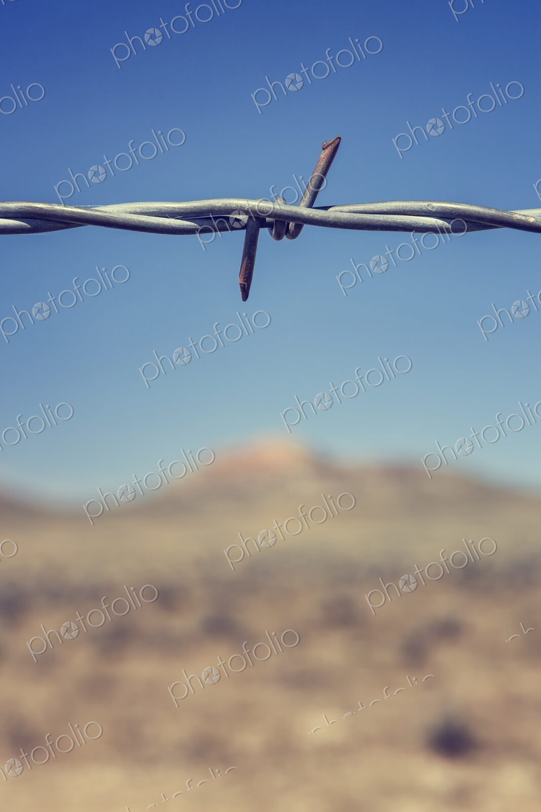 Close-up of a barbed wire fence with sharp focus on the twisted metal against a…