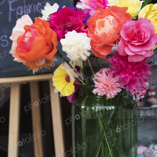 Close up of a bunch of colourful handcrafted fabric flowers in a vase.