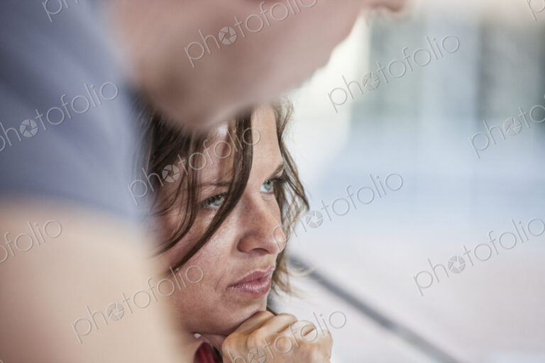 Close-up of a caucasian woman in an office meeting and a colleague standing over her.