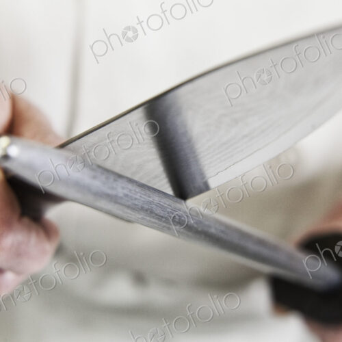Close-up of a chef sharpening a large kitchen knife blade with a steel.