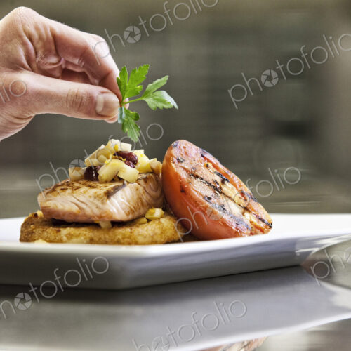 Close-up of a chef's hands adding a garnish to a salmon dinner plate. Close-up of a chef's hands adding a garnish to a salmon dinner plate.