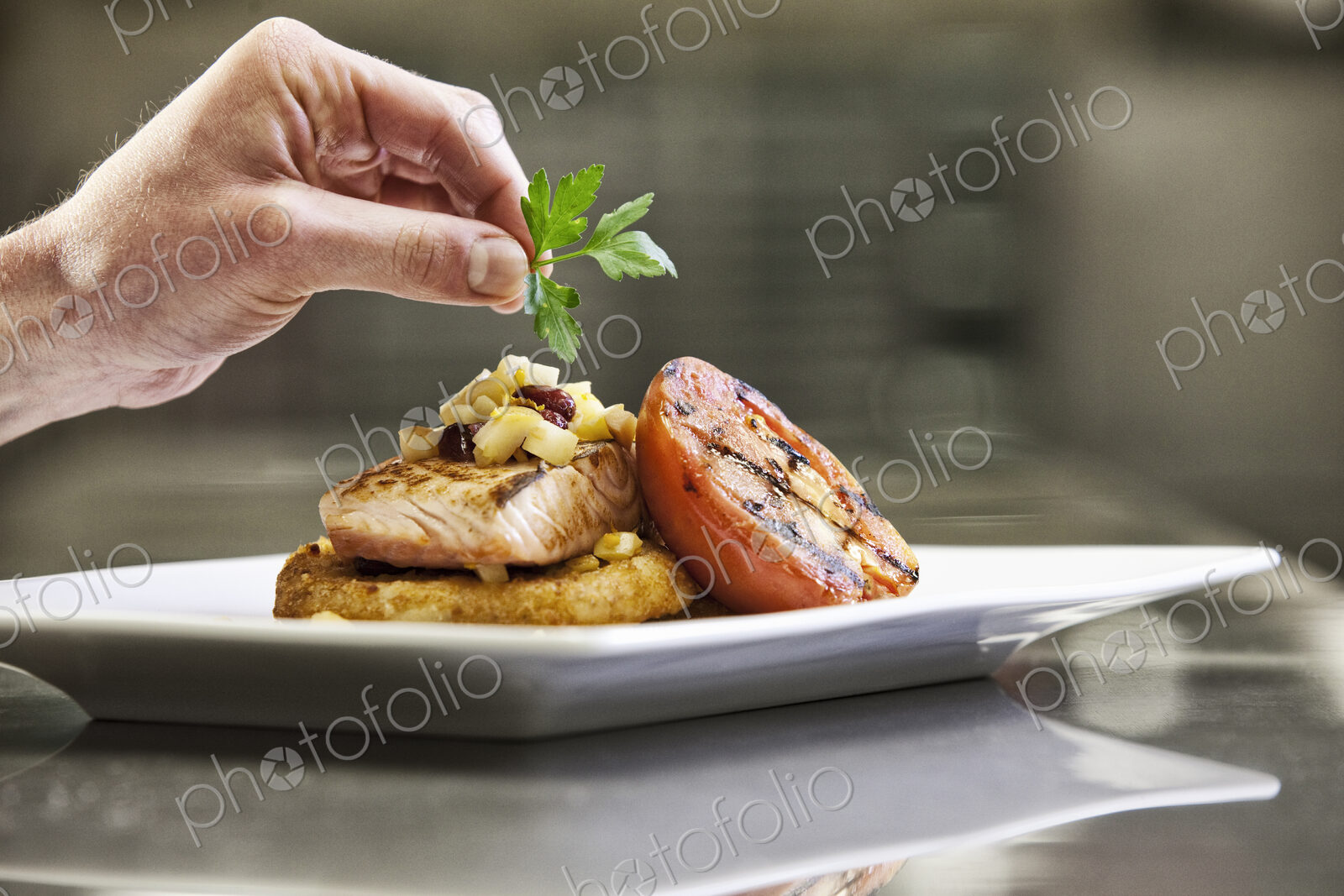 Close-up of a chef’s hands adding a garnish to a salmon dinner plate.