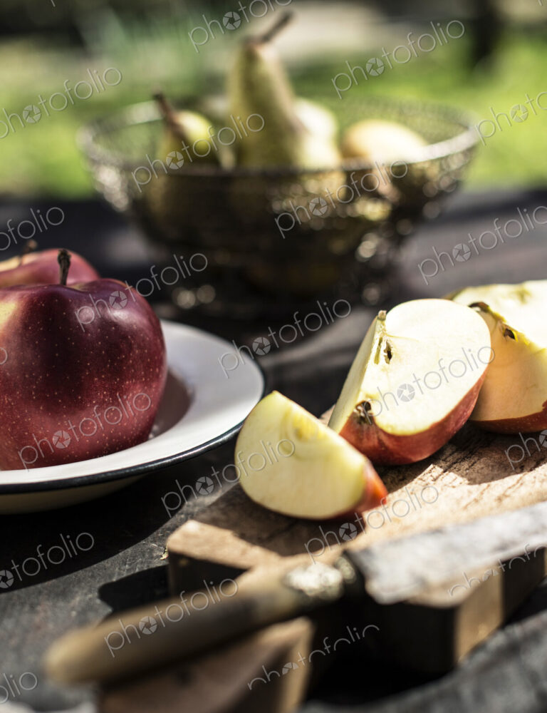 Close up of a cut apple and knife on rustic wooden board on a table outside.