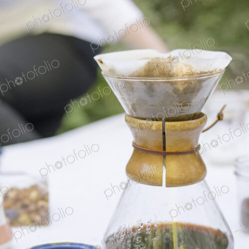Close up of a glass coffee maker on a table in a garden.