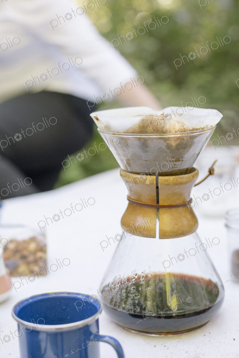 Close up of a glass coffee maker on a table in a garden.