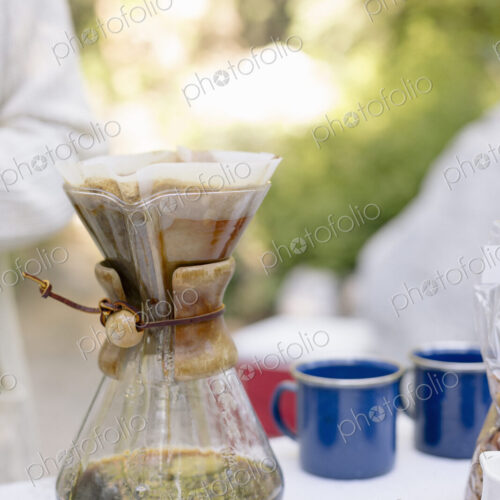 Close up of a glass coffee maker on a table in a garden.