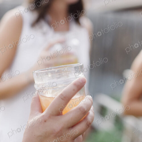 Close up of a hand holding a drink, a woman in the background. Close up of a hand holding a drink, a woman in the background.