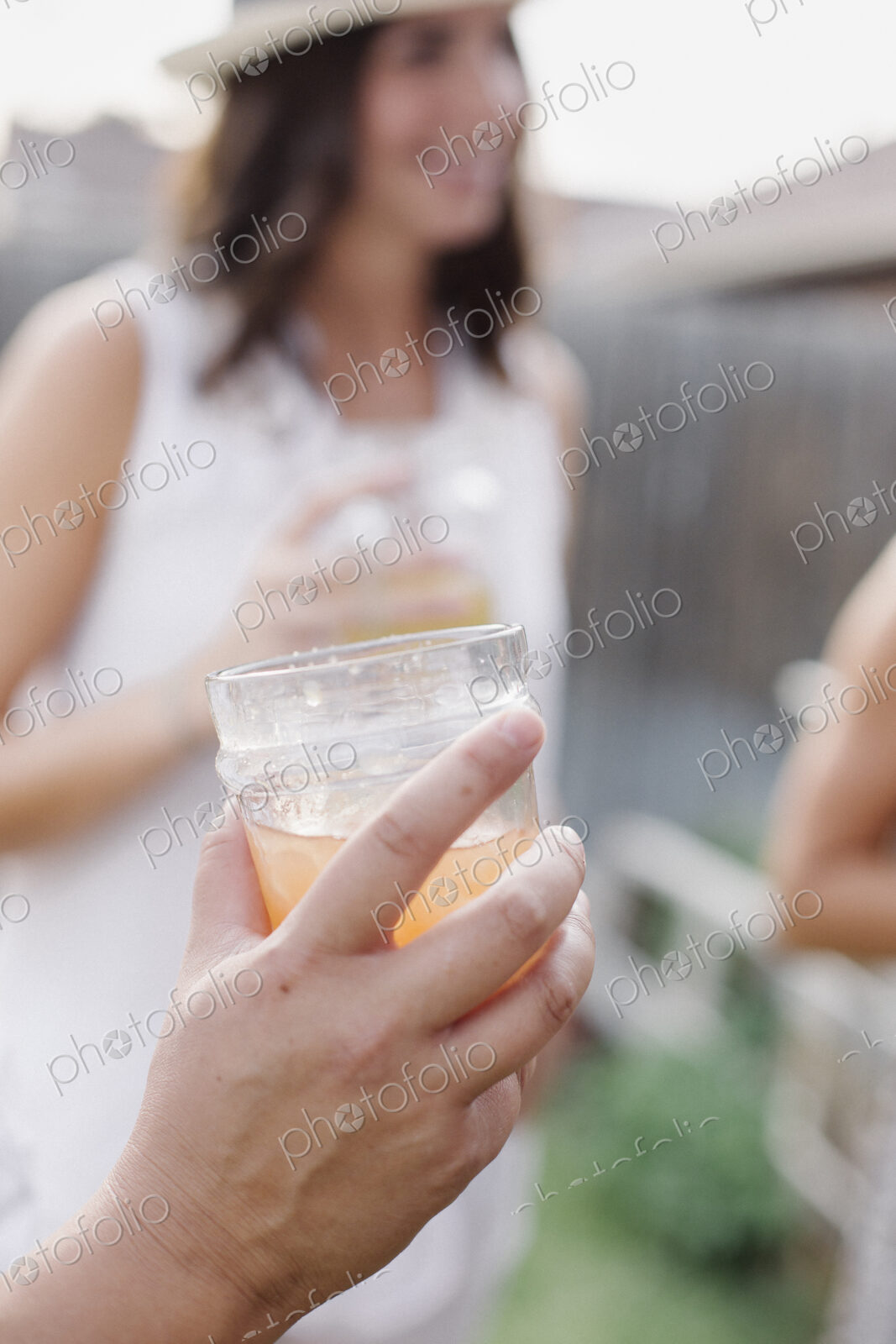 Close up of a hand holding a drink, a woman in the background.