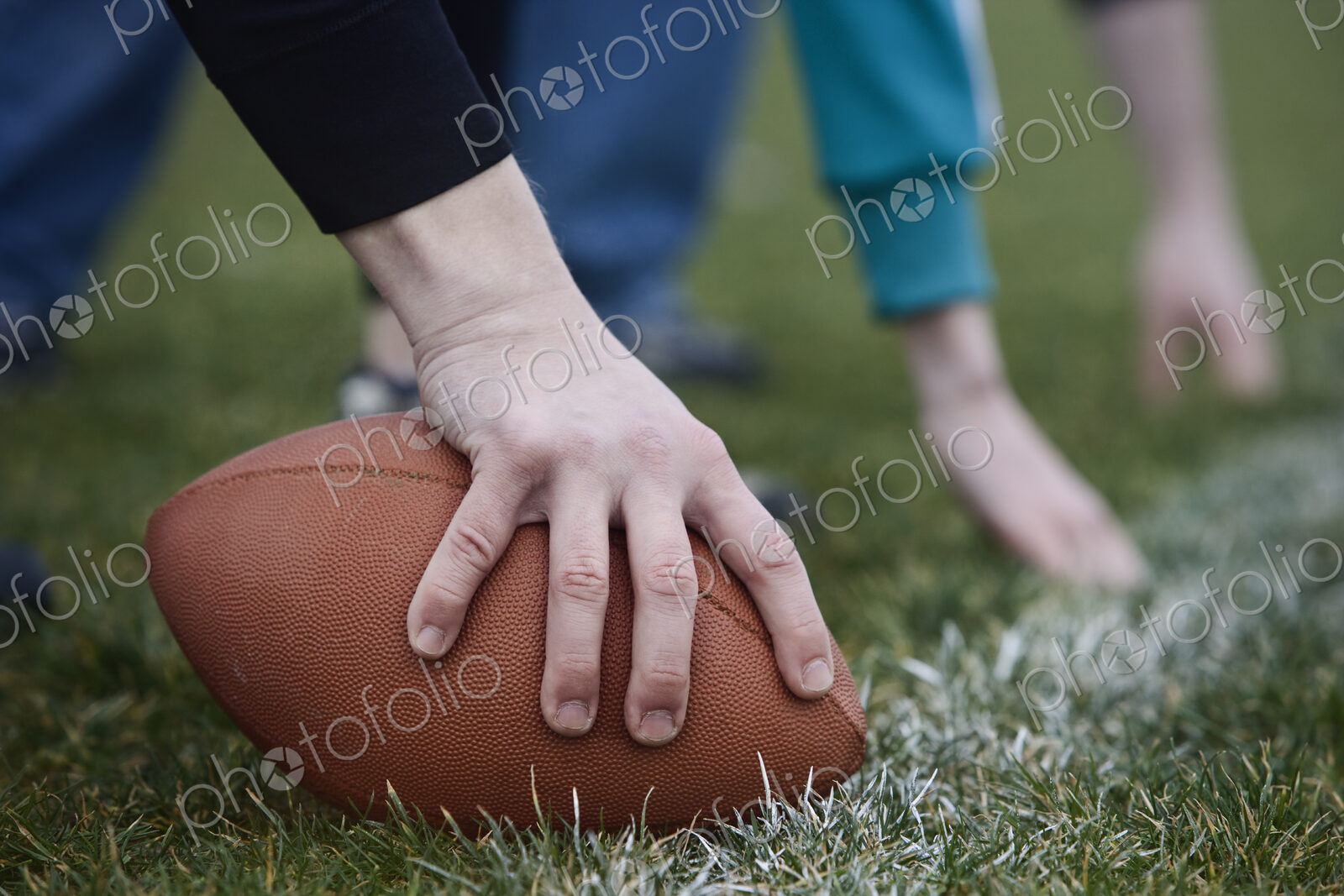 Close up of a hand holding an oval football on the line, during a game of non-contact…