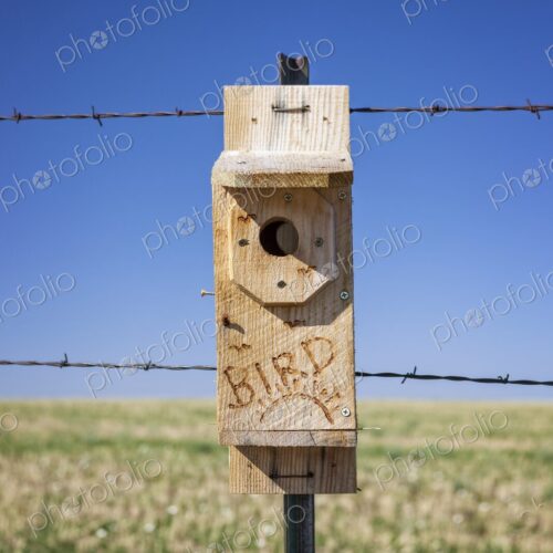 Close-up of a handmade wooden birdhouse mounted on a rural fence post with barbed… Close-up of a handmade wooden birdhouse mounted on a rural fence post with barbed…