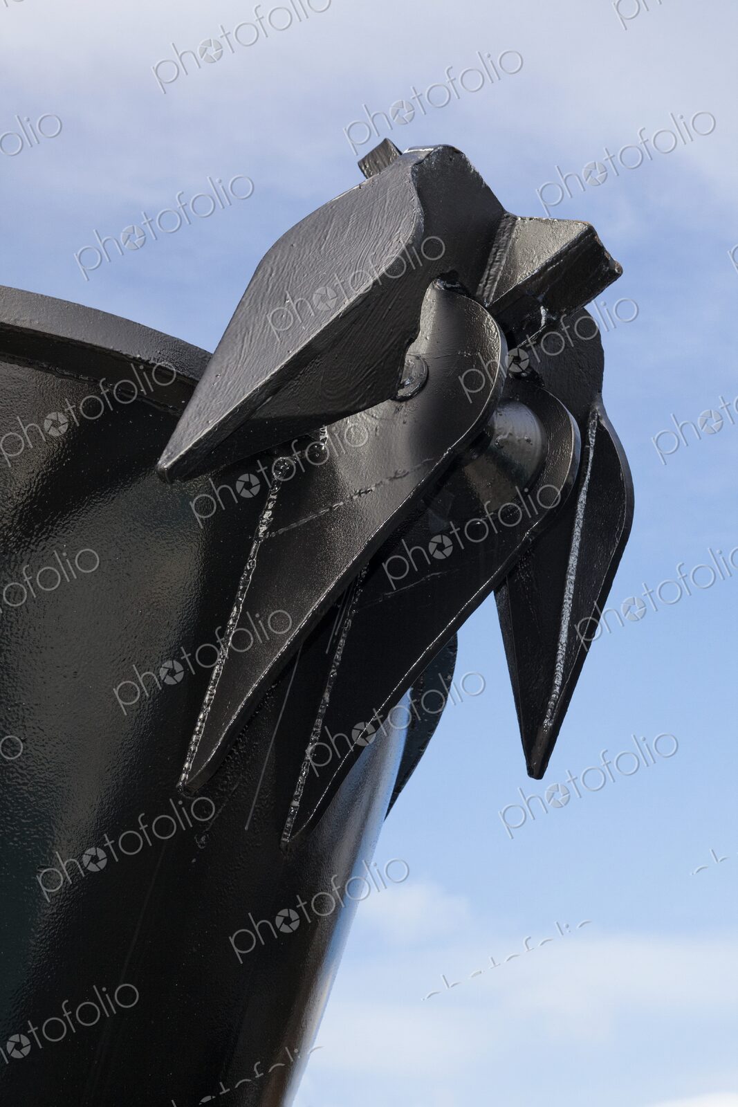 Close-up of a large black anchor mounted on the bow of a ship, the sharp lines and…