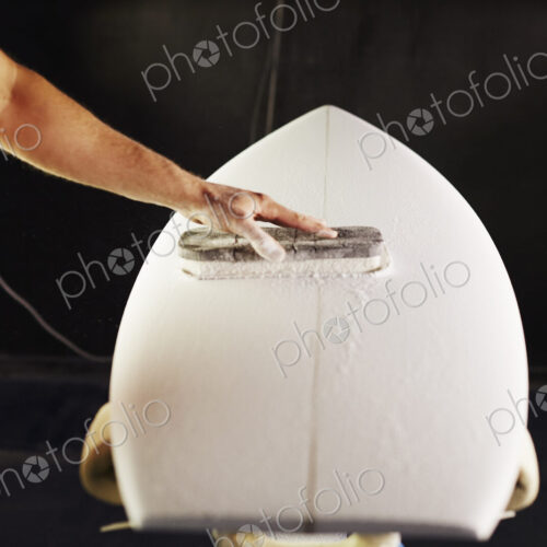 Close up of a man sanding a surfboard in a workshop.