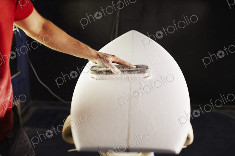Close up of a man sanding a surfboard in a workshop.