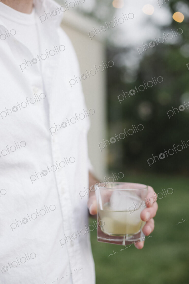 Close up of a man standing in a garden, holding a drink.