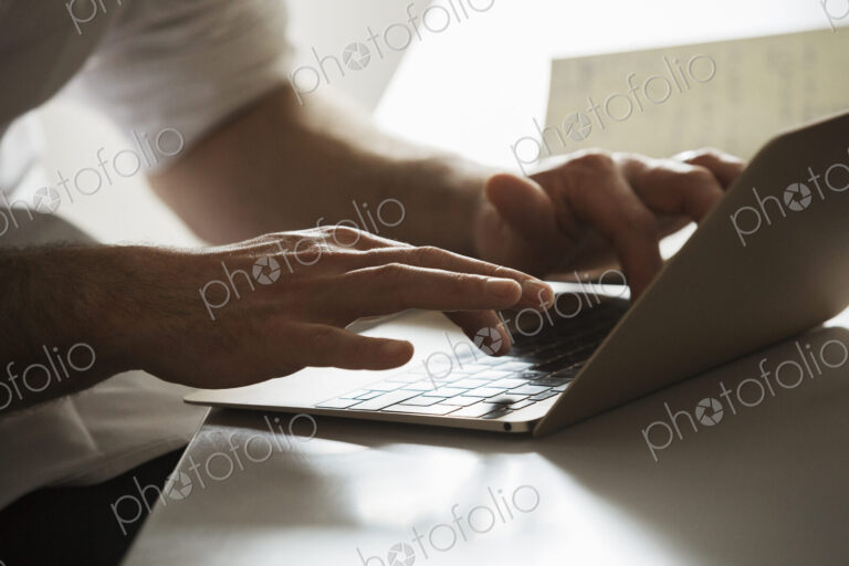 Close up of a man working on a laptop computer, typing.