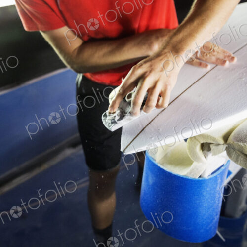 Close up of a man working on a surfboard in a workshop.