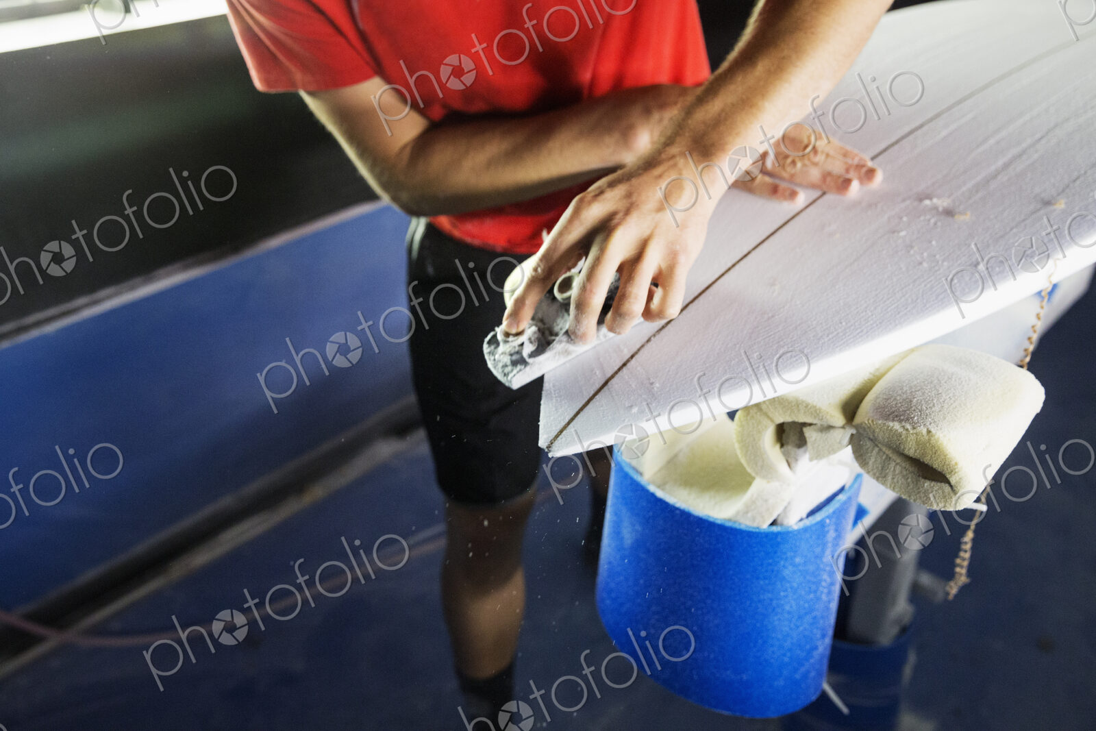 Close up of a man working on a surfboard in a workshop.