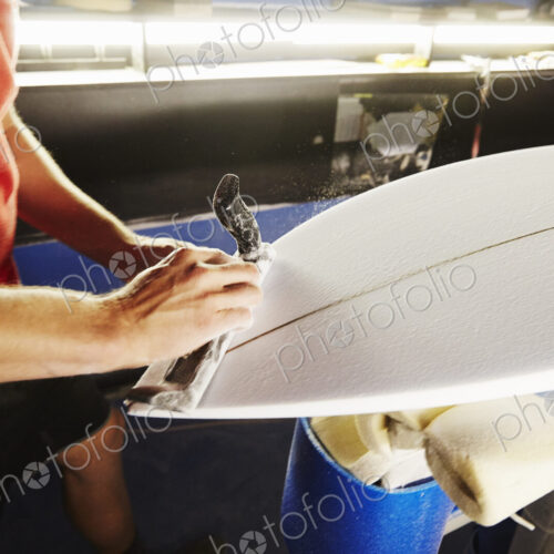 Close up of a man working on a surfboard in a workshop.