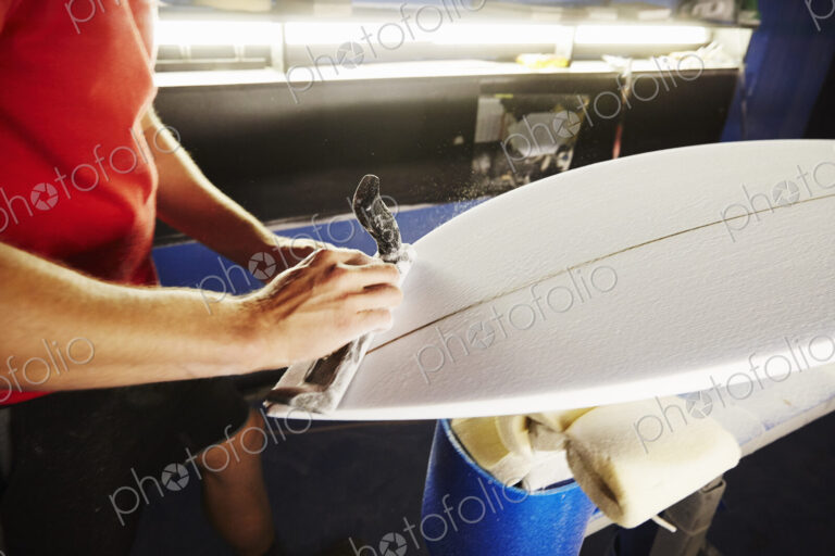 Close up of a man working on a surfboard in a workshop.