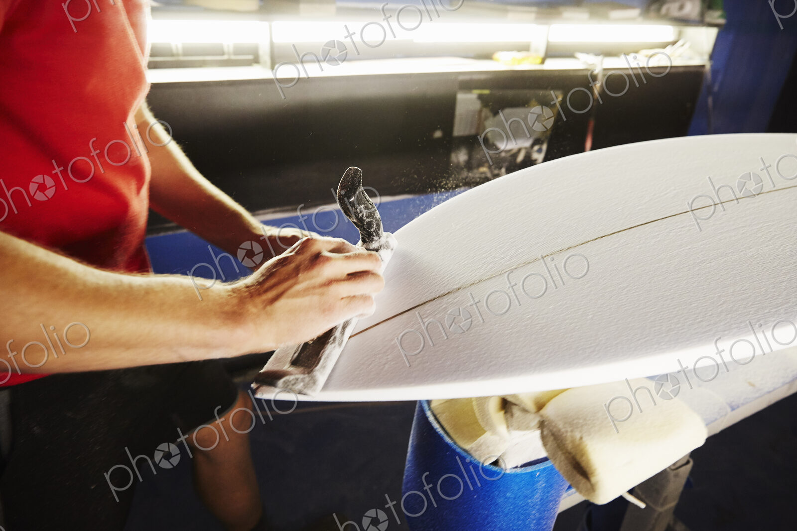 Close up of a man working on a surfboard in a workshop.
