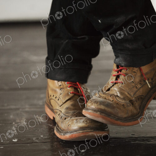 Close up of a man's feet, wearing brown brogues with red shoe laces.