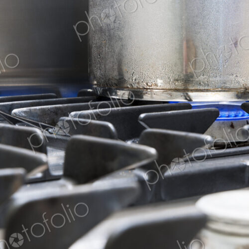 Close up of a metal pan on a gas hob, blue flames heating the pan.