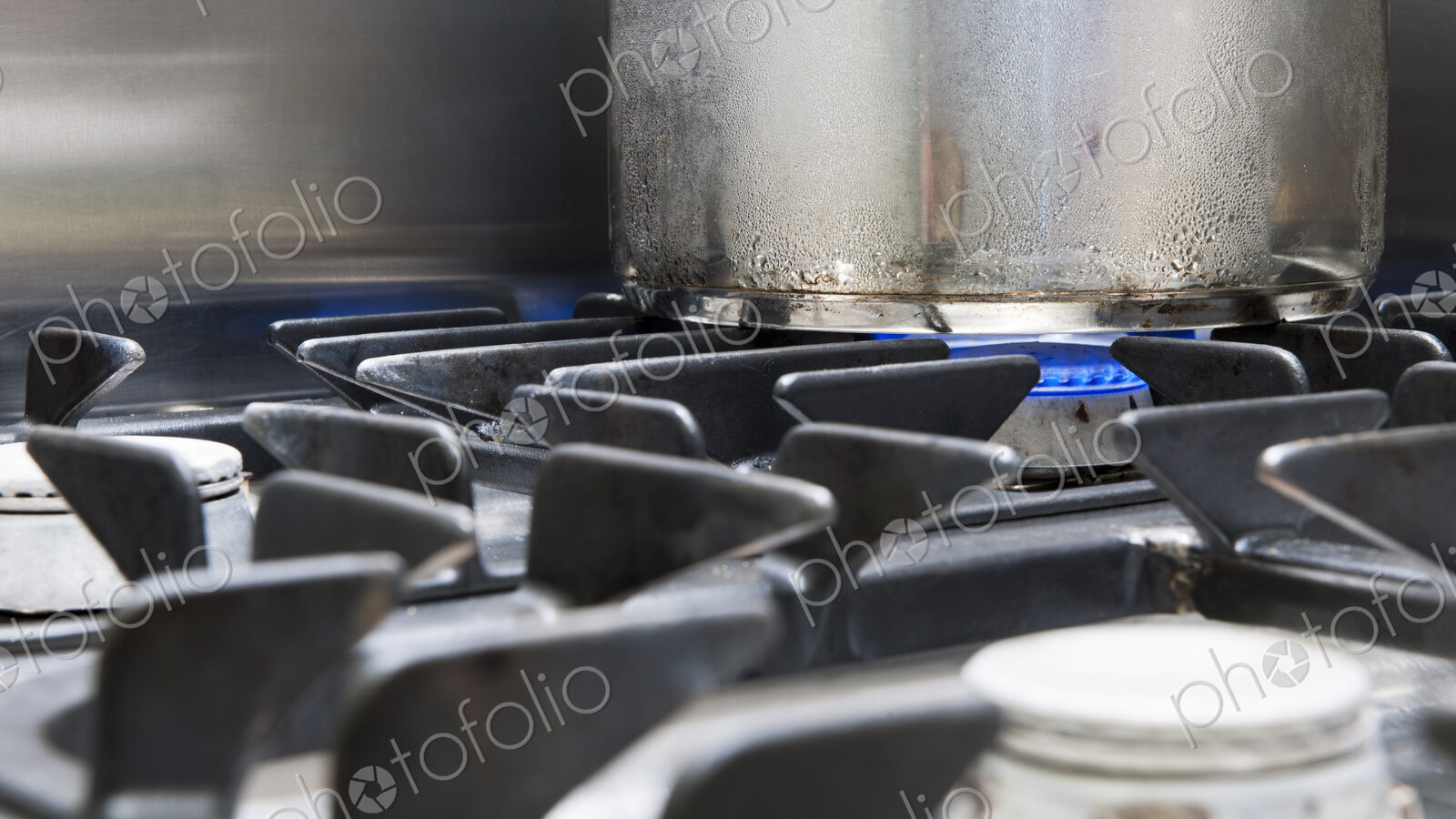 Close up of a metal pan on a gas hob, blue flames heating the pan.