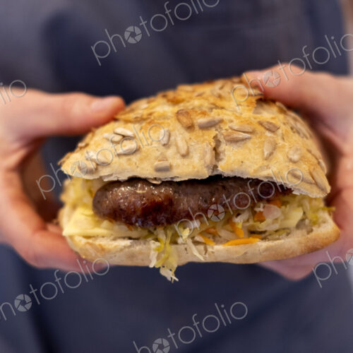 Close up of a person holding freshly made sausage bap, a seeded bun in an artisan bakery.