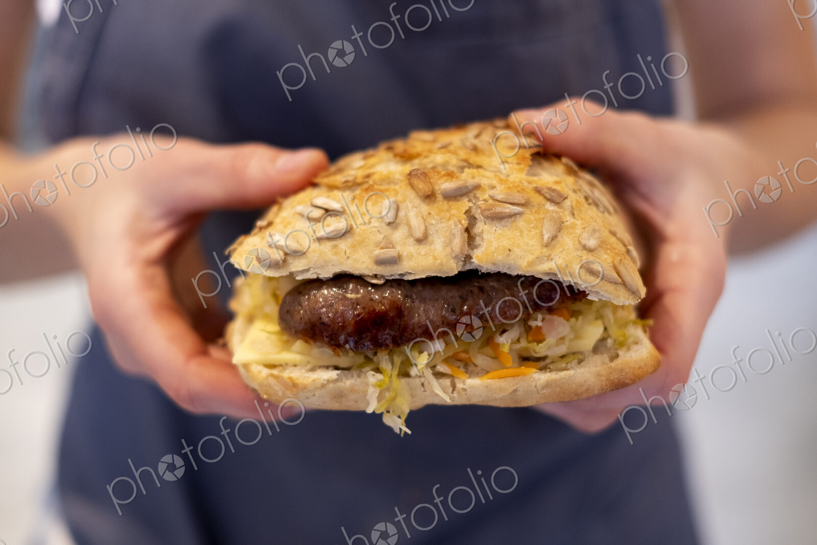 Close up of a person holding freshly made sausage bap, a seeded bun in an artisan bakery.