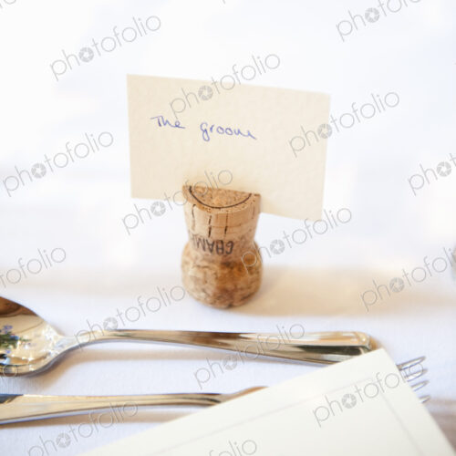 Close up of a place setting at the top table at a wedding banquet. An upside down cork… Close up of a place setting at the top table at a wedding banquet. An upside down cork…