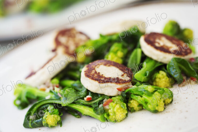 Close up of a plate of food, scallops and green vegetables.
