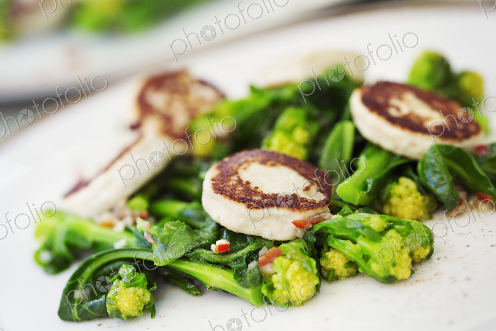Close up of a plate of food, scallops and green vegetables.