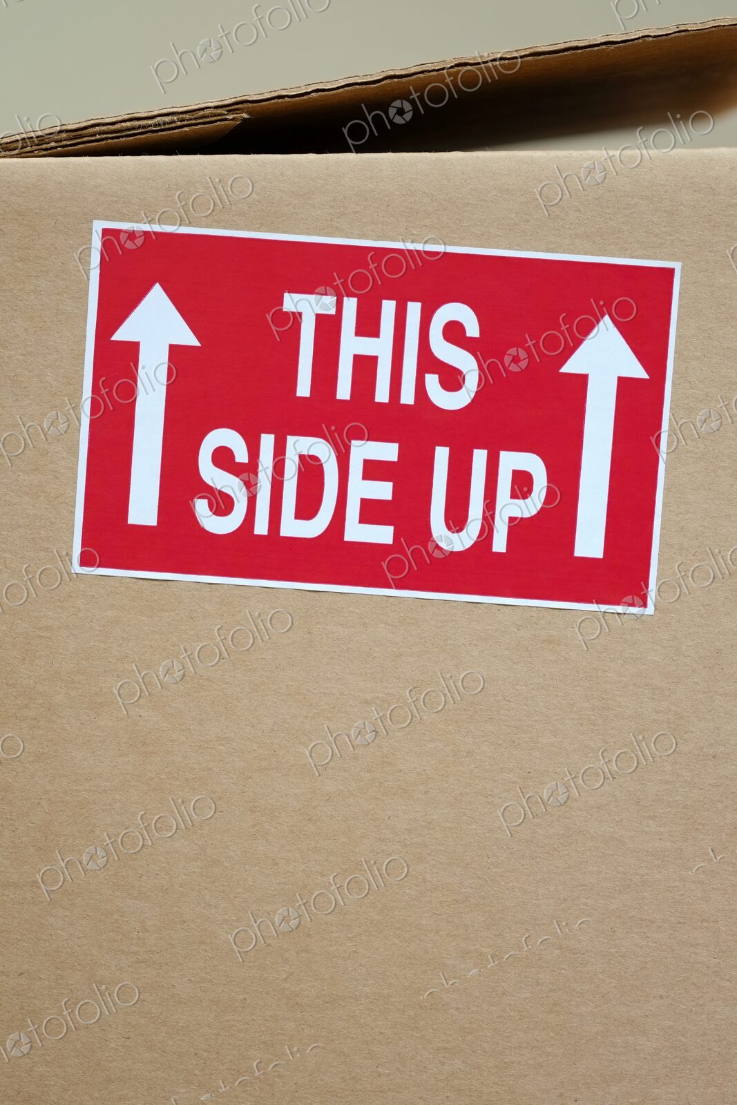 Close-up of a red “This Side Up” sticker with white arrows on a cardboard shipping box…