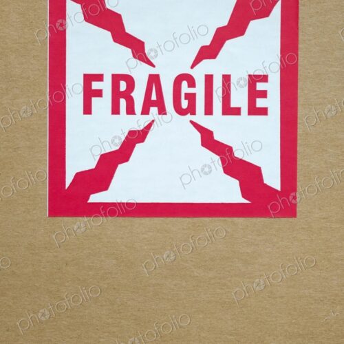 Close-up of a red and white "Fragile" sticker with crack-like graphic elements on a…