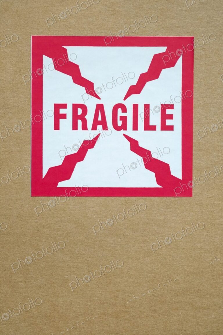 Close-up of a red and white "Fragile" sticker with crack-like graphic elements on a…